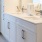 Large well lit bathroom with large mirror and white cabinets with a spacious walk in closet.